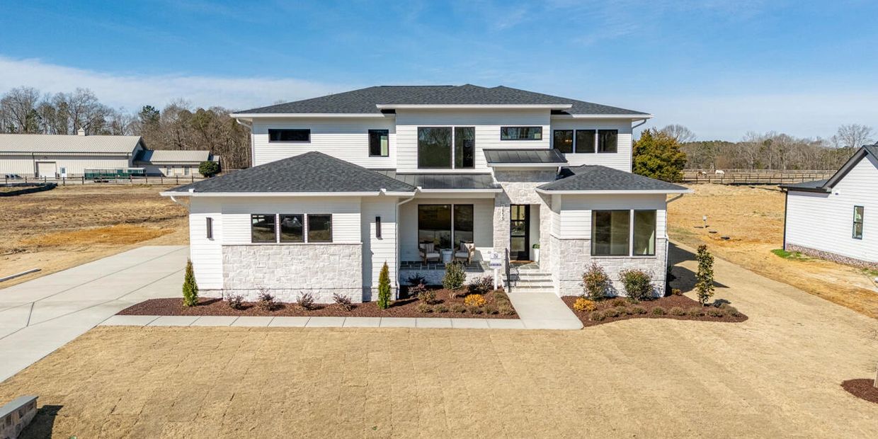 Modern two-story house with white exterior and dark roof under clear blue sky.