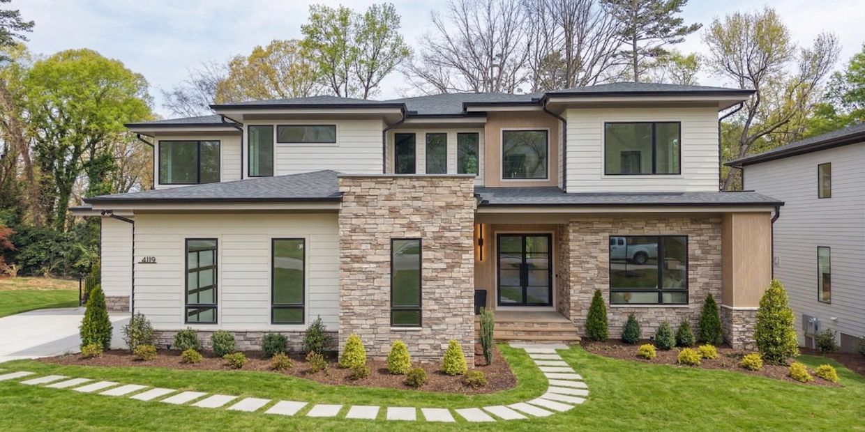 Modern two-story house with stone and siding exterior, surrounded by greenery.