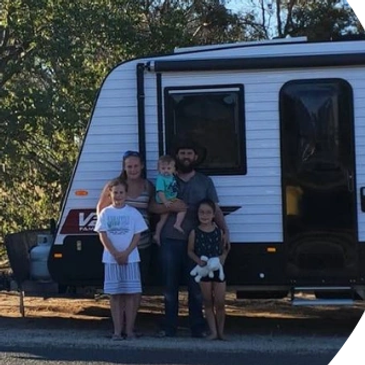 Family of five posing in front of a camper trailer outdoors.