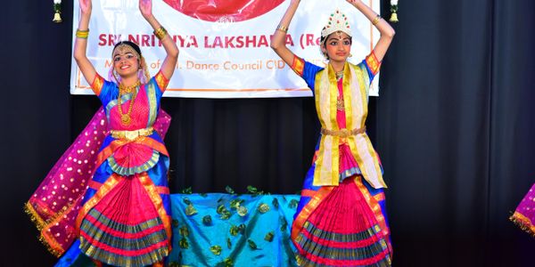 Two dancers perform traditional Indian dance in colorful attire on stage.