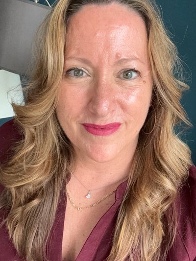 Smiling woman with blonde wavy hair and burgundy top.