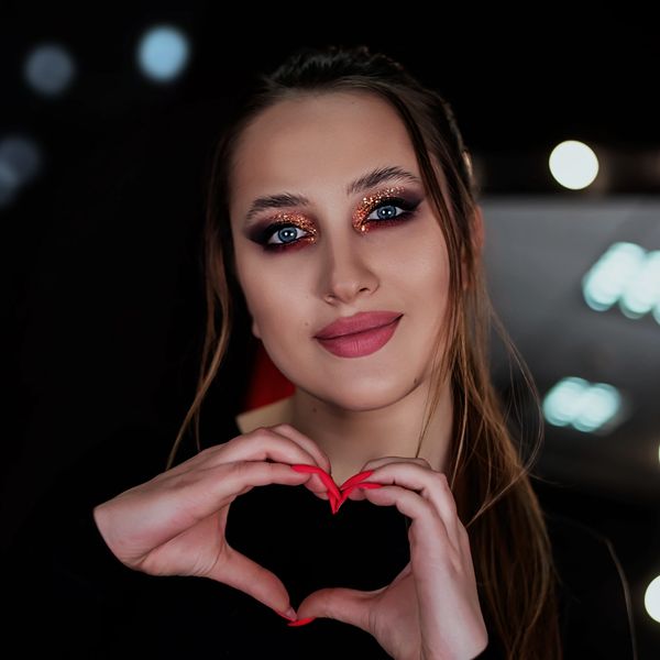 Woman with glittery eye makeup making a heart with her hands.