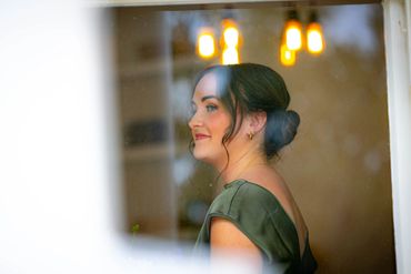 A woman with a green dress looks thoughtfully through a window.