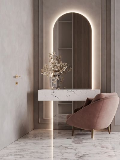 Elegant marble console with backlit arched mirror and pink velvet chair in a modern hallway.