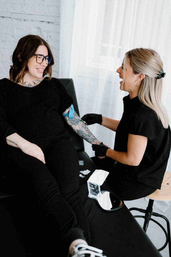 A woman with tattoos getting a blood draw from a smiling healthcare worker.