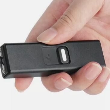 Hand holding a small black electronic device with a button.