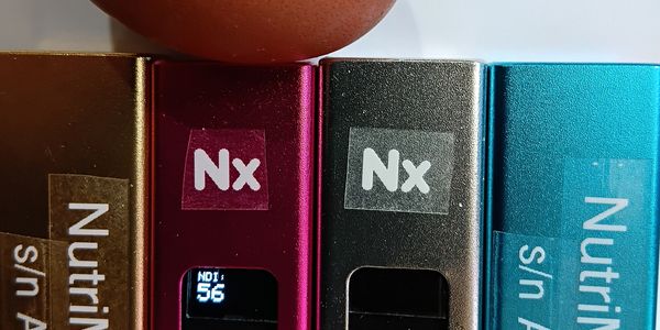 Close-up of labeled electronic devices with "Nx" stickers and a brown egg on top.