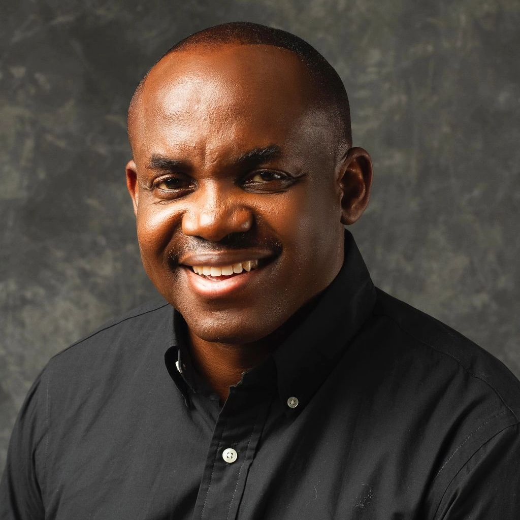 Smiling man in a black shirt against a textured backdrop.