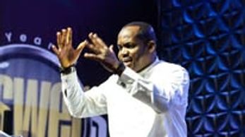 A man passionately speaking on stage with a dark blue backdrop.