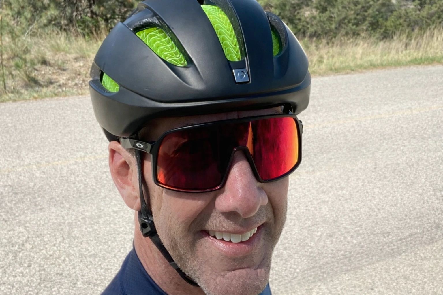 Man wearing a black and green cycling helmet with red reflective sunglasses.