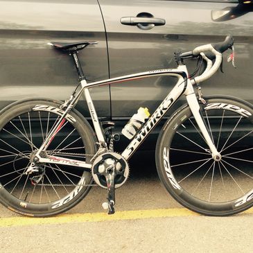 A sleek S-Works road bike leaning against a car on the street.