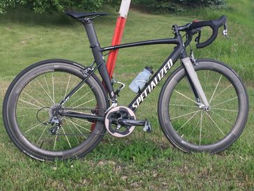 A black Specialized road bike with deep-section wheels parked on grass.