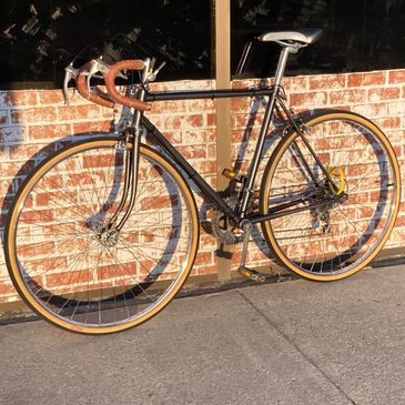 Classic road bike with brown handlebar tape leaning against a brick wall.