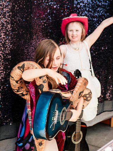 Two girls with guitars, one wearing a snake prop and the other a red hat.