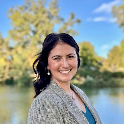Smiling woman outdoors with trees and water behind.