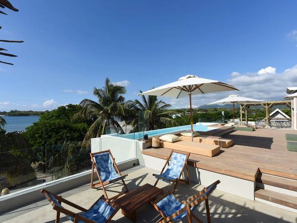 Relaxing outdoor terrace with lounge chairs and umbrellas overlooking tropical greenery and water.