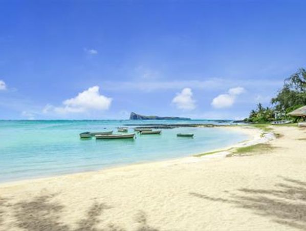 Tranquil beach with clear blue water and boats floating gently.