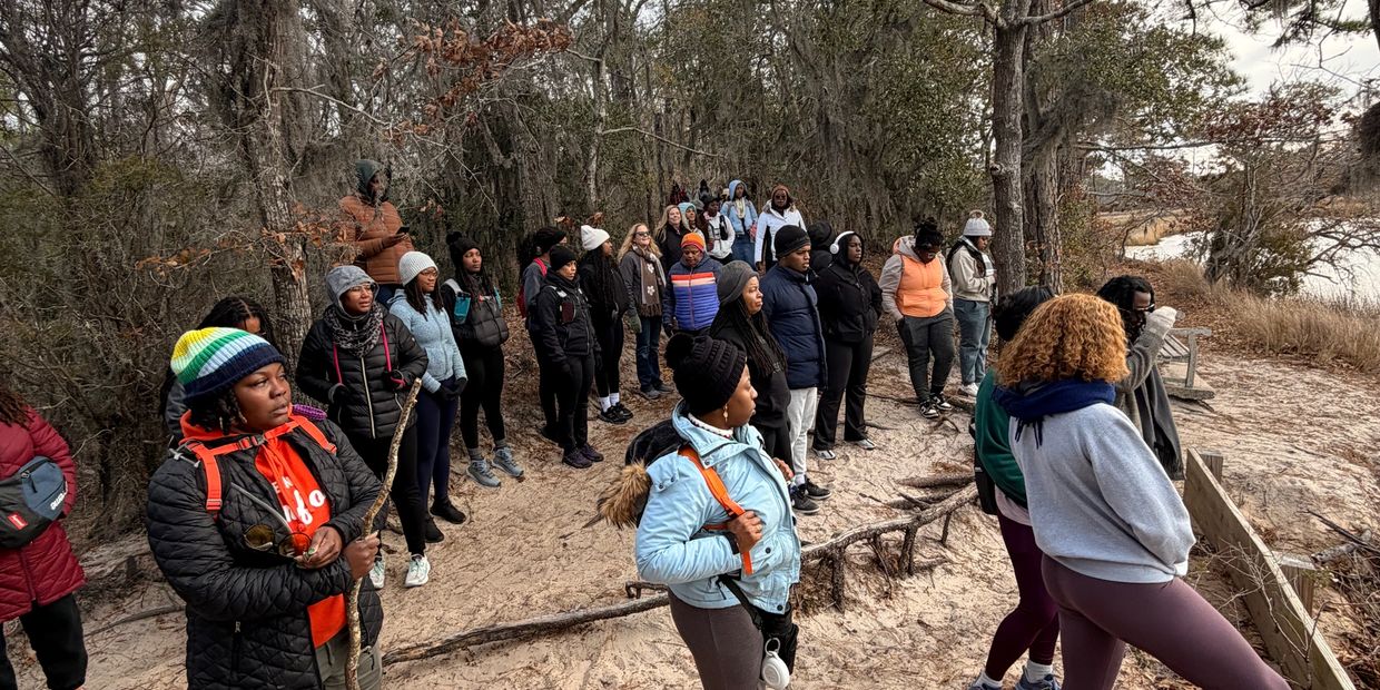 Group of people standing outdoors in a wooded area during a chilly day.