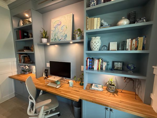 Modern home office with blue shelves, wooden desk, and decorative items.