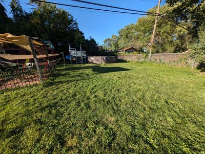 A backyard with grass, a swimming pool, and a play structure under a clear blue sky.