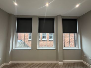 Three windows with black roller blinds in a modern room.