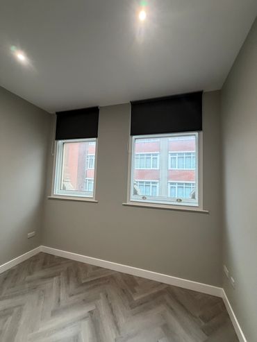 Empty room with two windows and dark blinds in a modern building.