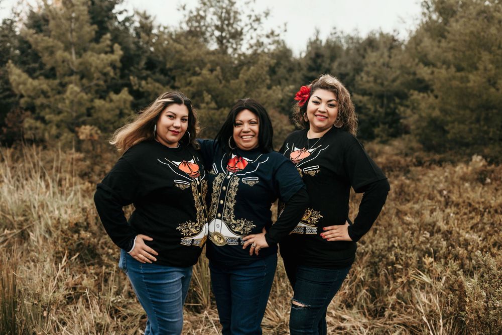 Maria and her two daughters smiling together in matching traditional shirts.