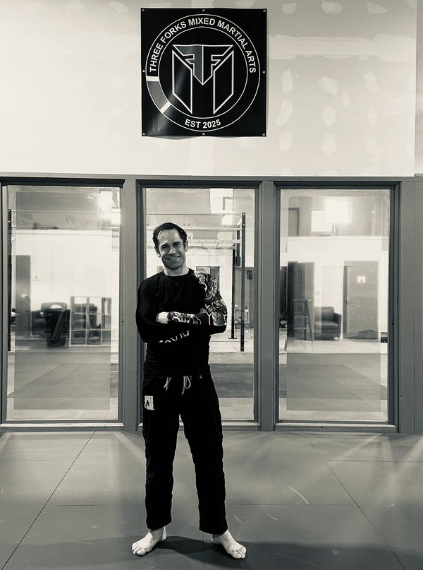 Martial artist standing confidently in a gym under a Three Forks Mixed Martial Arts banner.