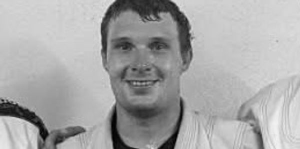 Man in a white martial arts gi smiling at the camera.