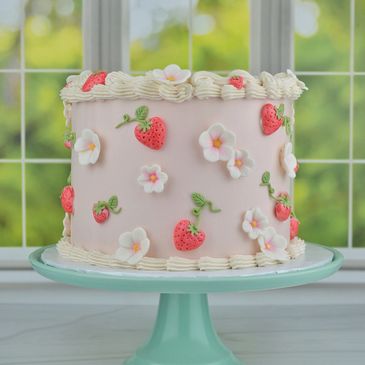 Pink cake decorated with strawberries and white flowers on a blue cake stand.