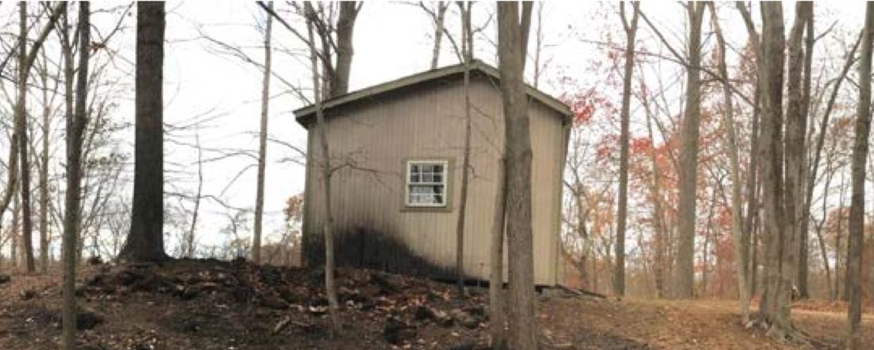 Small wood building at the top of a hill with one side partially burned from fire that spread up the