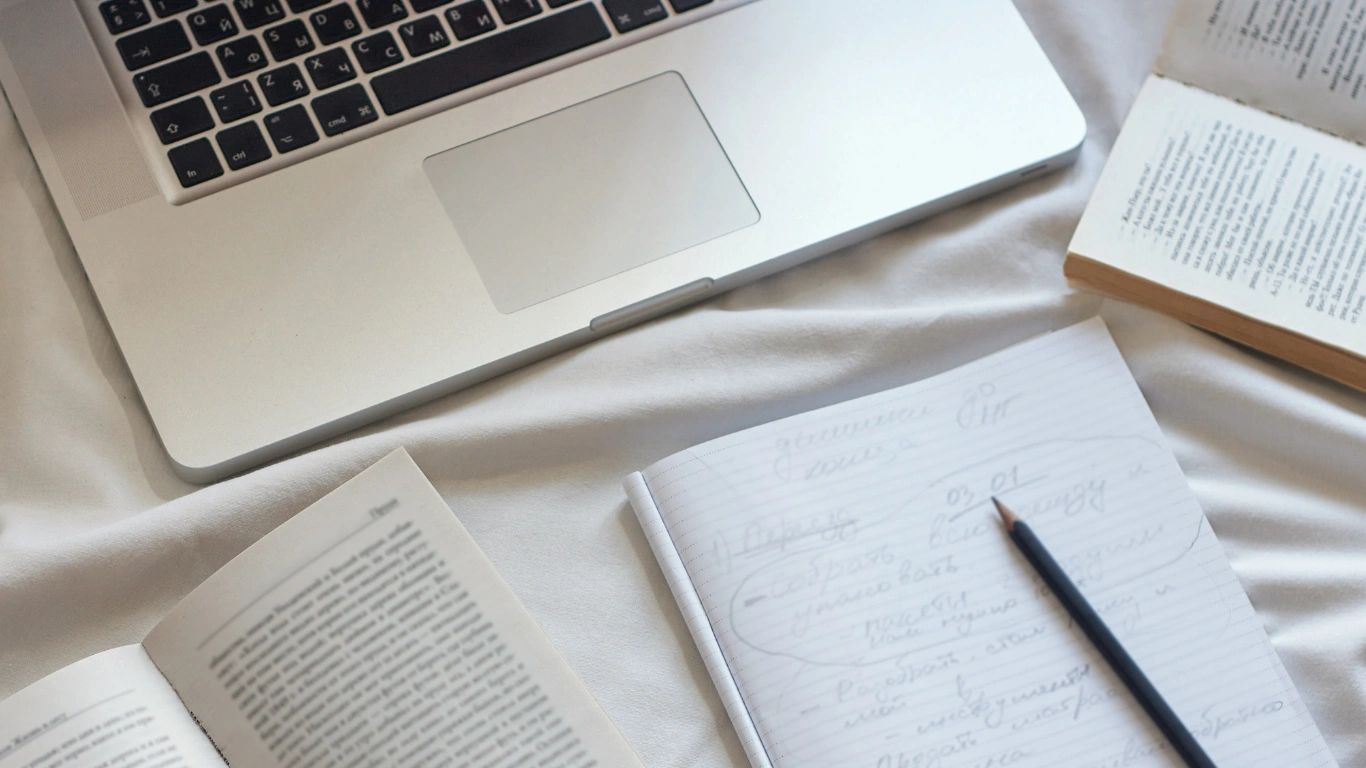 Study setup with laptop, open books, and handwritten notes on a white surface.