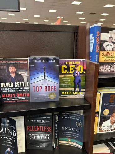 Books by Marty Smith and others on leadership and motivation displayed on a shelf.