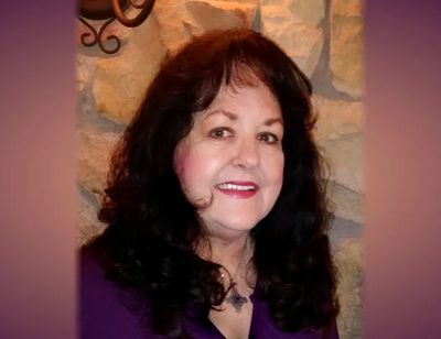 Smiling woman with dark hair in front of a stone wall.