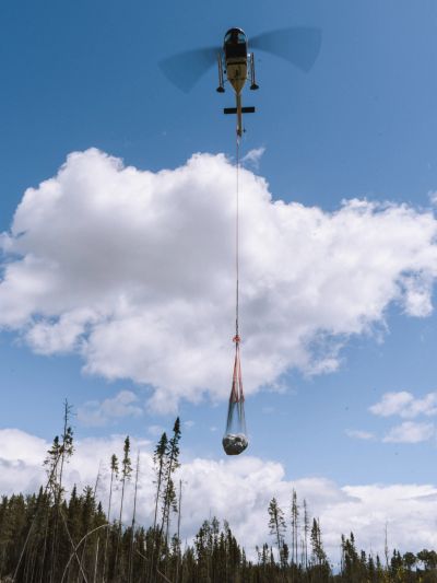 Helicopter transporting a large object over a forest under a blue sky.