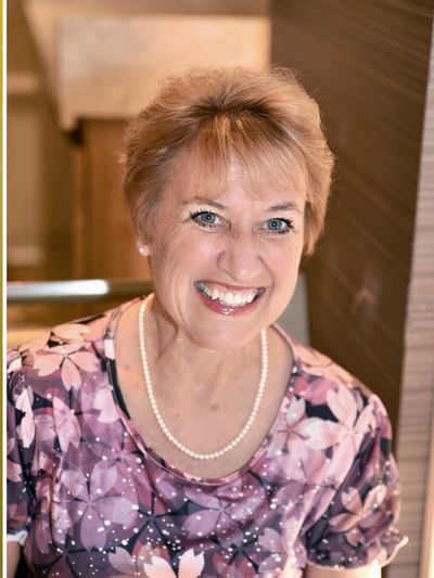 Smiling woman wearing a floral top and pearl necklace.