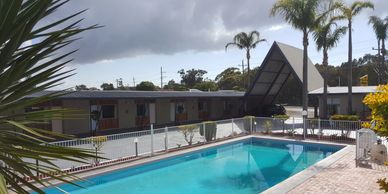 Outdoor swimming pool next to a motel with palm trees and cloudy sky.