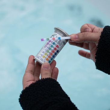 Hands holding a pool water testing kit with color comparison chart.