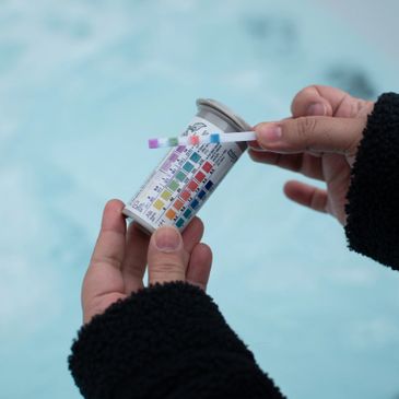 Hands holding a pool water testing kit with color comparison chart.