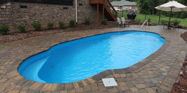 A clean backyard pool with brick surroundings and patio furniture.