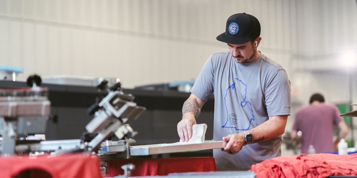 Complete Team Outfitter employee applying ink during the screen printing process.