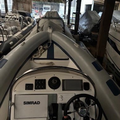 A white boat with a SIMRAD console docked inside a wooden shelter.