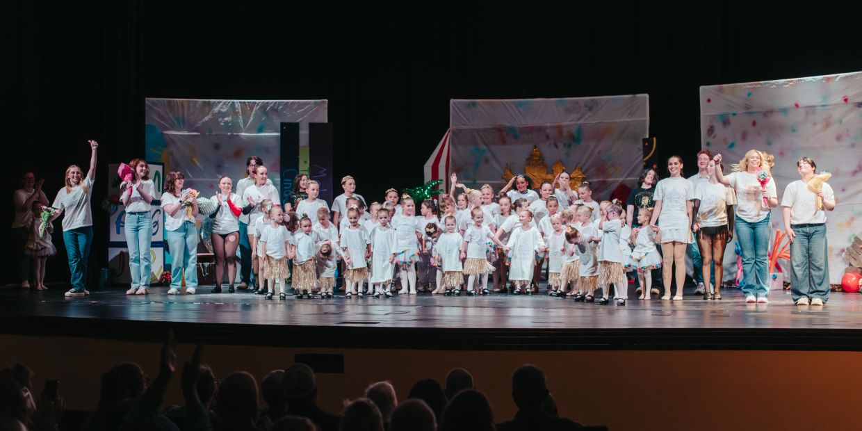 A large group of children and adults on stage during a performance curtain call.