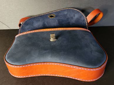 Open leather bag with orange sides and black flap on a dark surface.