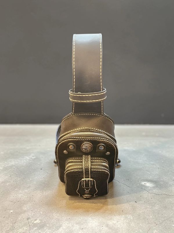 Black leather waist bag with white stitching on a concrete surface.
