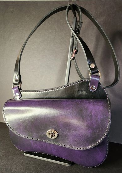 Elegant purple leather handbag with black strap and silver clasp.