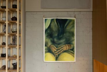 Abstract painting of hands resting on lap, hanging on a wall in a cozy room.