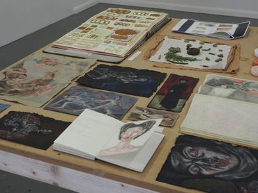 A table displaying various art pieces and sketches in a studio setting.