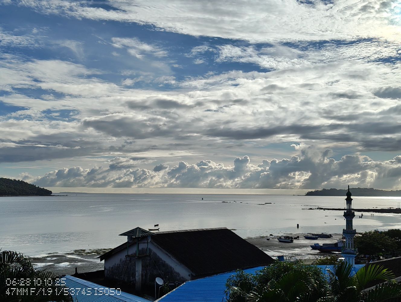 Calm coastal scene with boats, buildings, and dramatic cloudy sky.