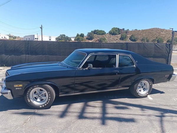 Classic black 1970s muscle car with polished wheels parked outdoors.